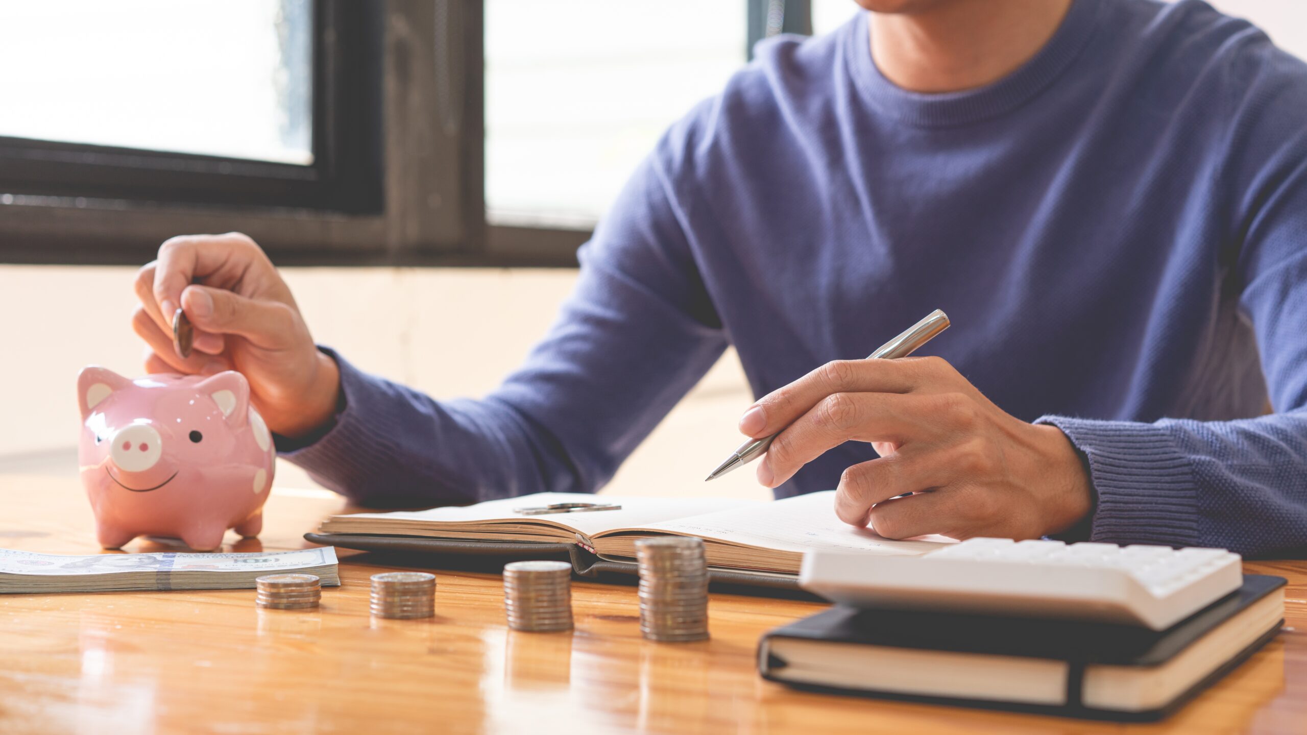 Conceptual image of a person sitting at a table with a piggy bank on how to save for your first home.