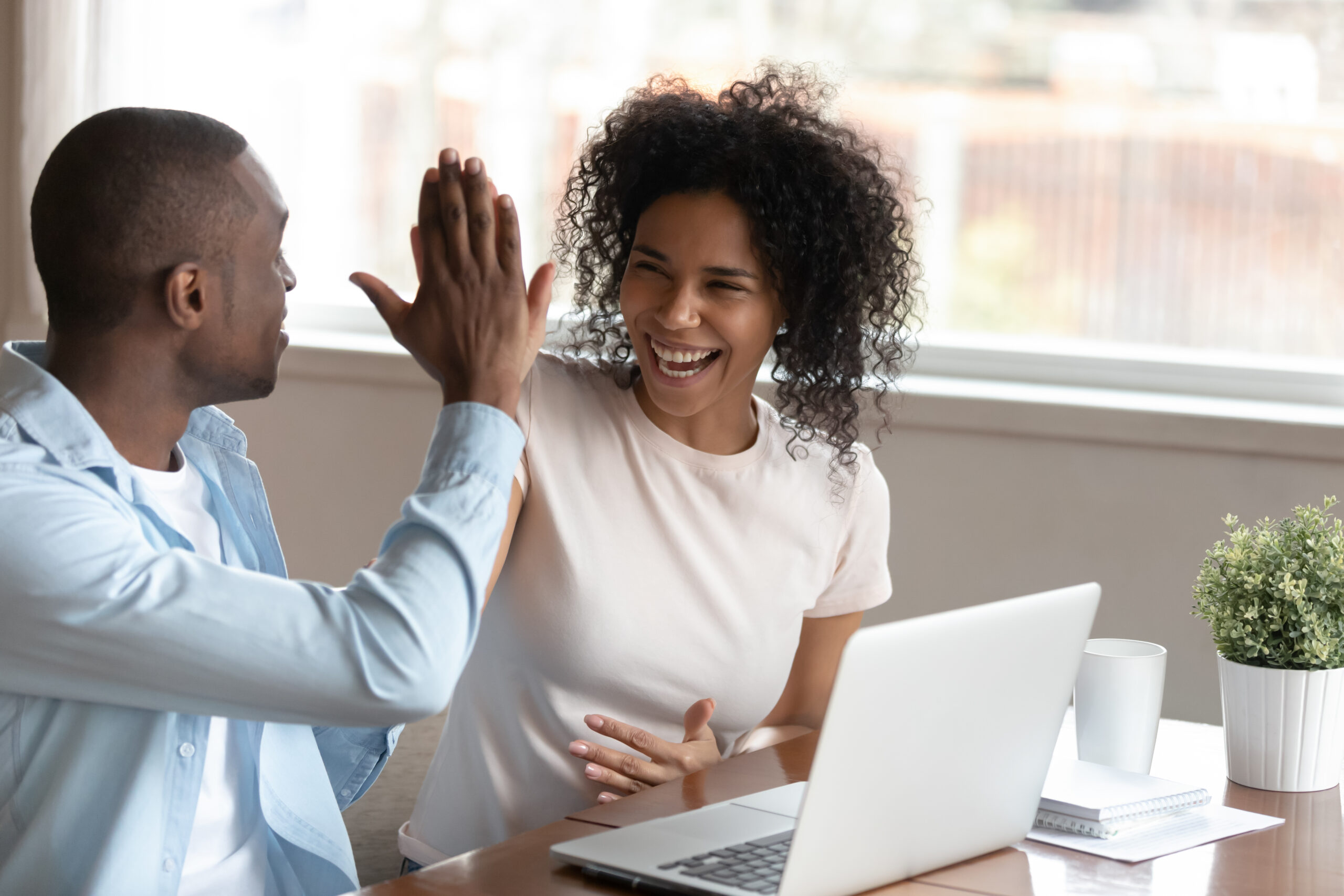 Husband and wife sitting at a table together giving each other a high-five, celebrating their mortgage approval