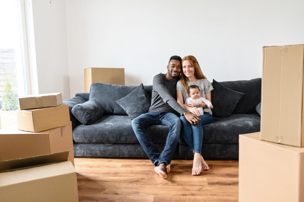 Couple sitting on couch holding baby surrounded by moving boxes