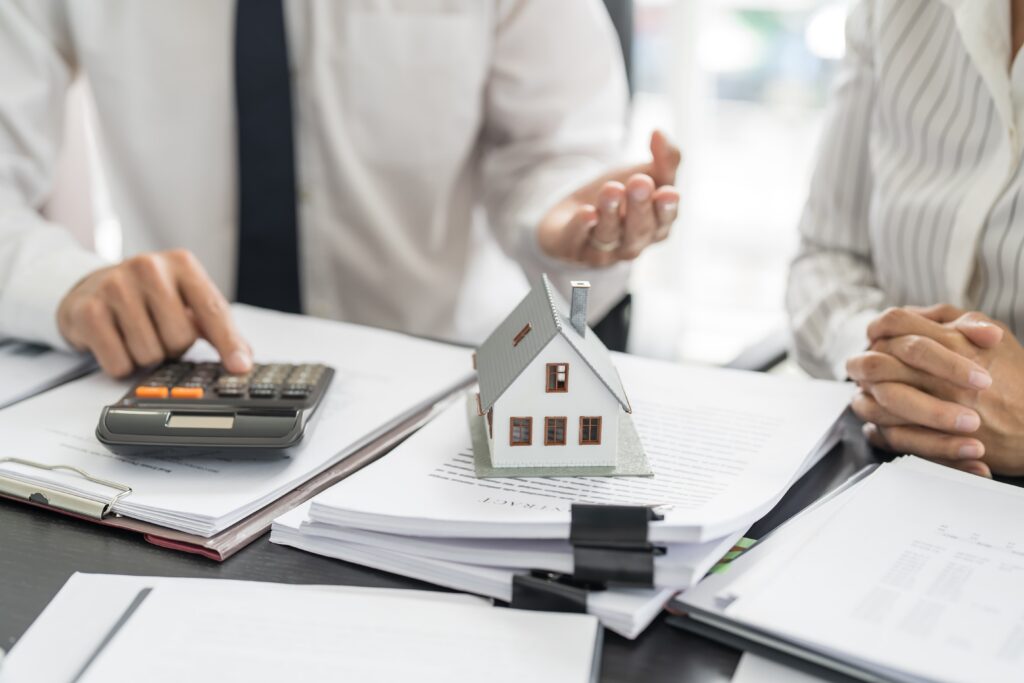 A desk with papers and a calculator on it with a small model house